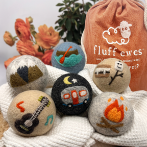 Six Fluff Ewes "Are we there yet?" Premium Wool Dryer Balls, eco-friendly and made from organic New Zealand wool, with camping-themed designs, displayed in front of a "fluff ewes" drawstring bag.