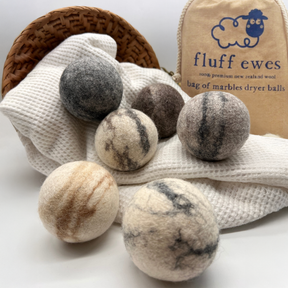 Six Fluff Ewes "Bag of Marbles" premium dryer balls—dye-free and made from 100% natural marbleized sheep's wool—sit on a white cloth, with a basket and branded bag in the background. Set includes 6 eco-friendly laundry essentials.