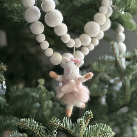 The Ballet Mouse, a handmade wool ornament in a pink dress, hangs on a Christmas tree decorated with white felt garland.