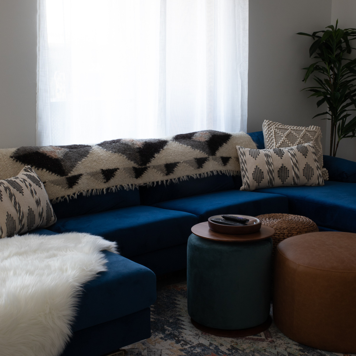 A blue sectional sofa with patterned pillows, two ottomans, a potted plant by a window, and the Iskara (Spark) Wool Bed/Couch Runner draped over the couch.