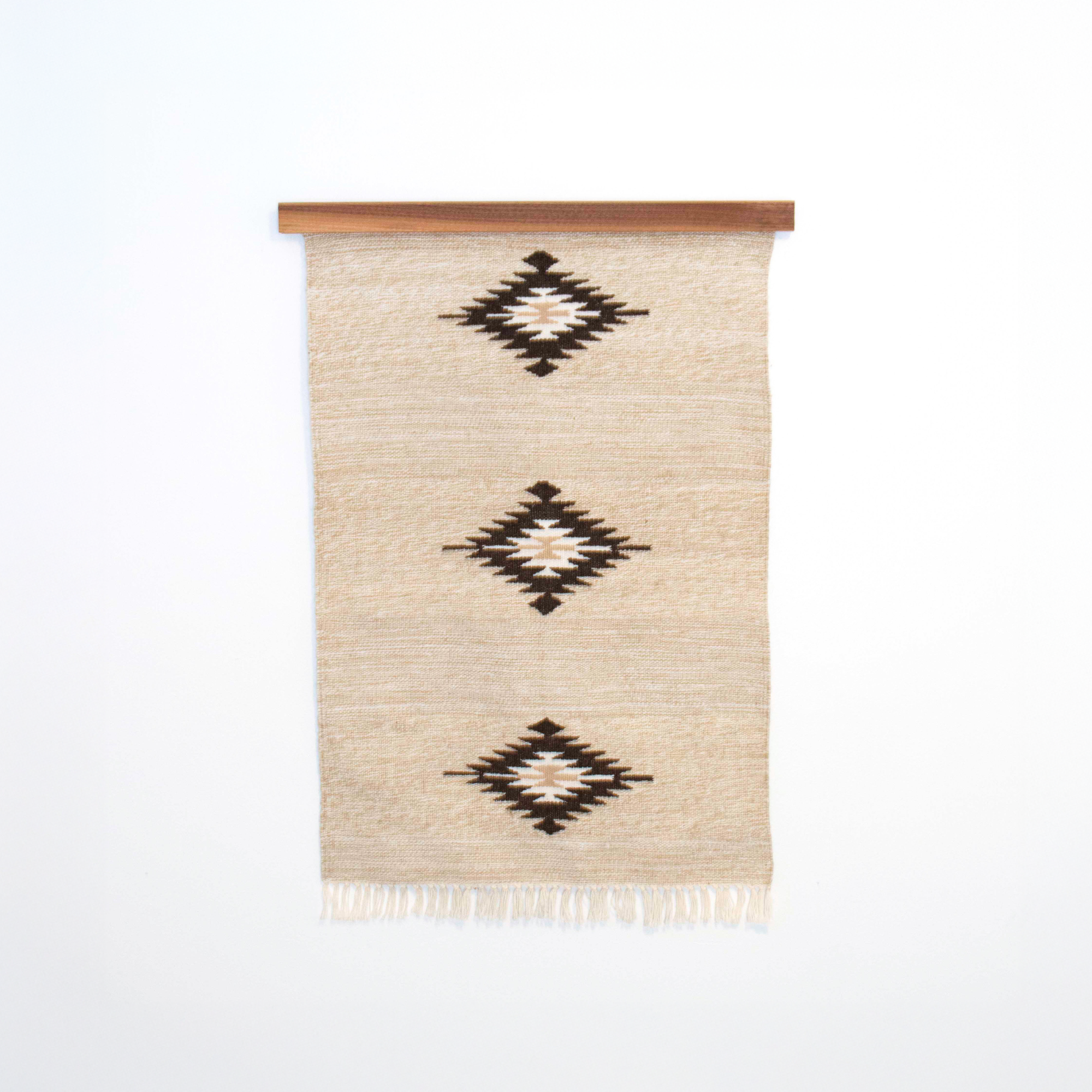Chitki (Crisp) Wool Rug / Wall Hanging ($240) features a beige base with three black diamond patterns and comes with a wood hanger, crafted in an eco-friendly mill for a natural, artisan touch.