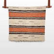 The Chudovo (Well) Wool Statement Throw / Baby Blanket, featuring orange and black horizontal stripes, hangs on a rod against a white background.