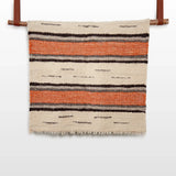 The Chudovo (Well) Wool Statement Throw / Baby Blanket, featuring orange and black horizontal stripes, hangs on a rod against a white background.