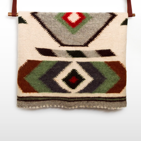 The Diamant (Diamond) Wool Statement Bed Blanket, featuring geometric patterns in green, brown, gray, black, and red, hangs on a rod—ideal for cozy winter decor or as an authentic Carpathian Mountain accent.