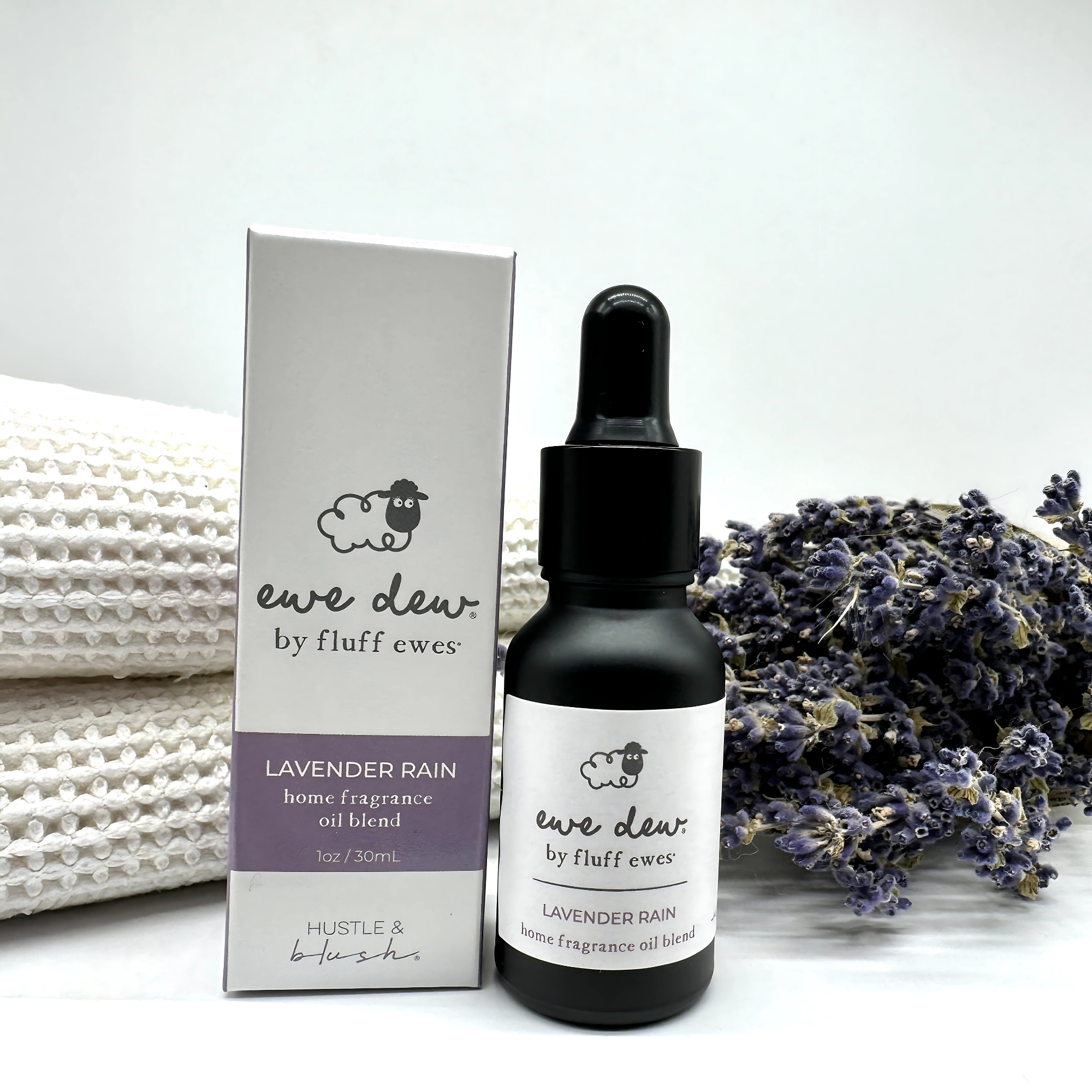 Ewe Dew by Fluff Ewes Lavender Rain Laundry, Home Fragrance + Aromatherapy Essential Oil Blend (Lavender Citrus Scent), 0.5 fl oz, perfect for wool dryer balls or oil diffusers, shown with lavender sprigs and towels in the background.