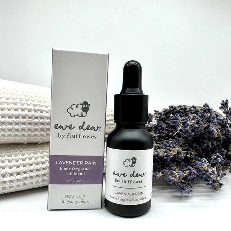 Ewe Dew by Fluff Ewes Lavender Rain Laundry, Home Fragrance + Aromatherapy Essential Oil Blend (Lavender Citrus Scent), 0.5 fl oz, perfect for wool dryer balls or oil diffusers, shown with lavender sprigs and towels in the background.
