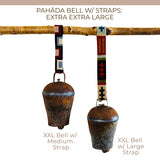 Two vintage handmade Pahāḍa bells from the Himalayan mountains of Nepal and Tibet hang from a branch, each with a colorful patterned strap. Perfect as Christmas ornaments, wreath decor, or for sound baths; each bell measures 11".