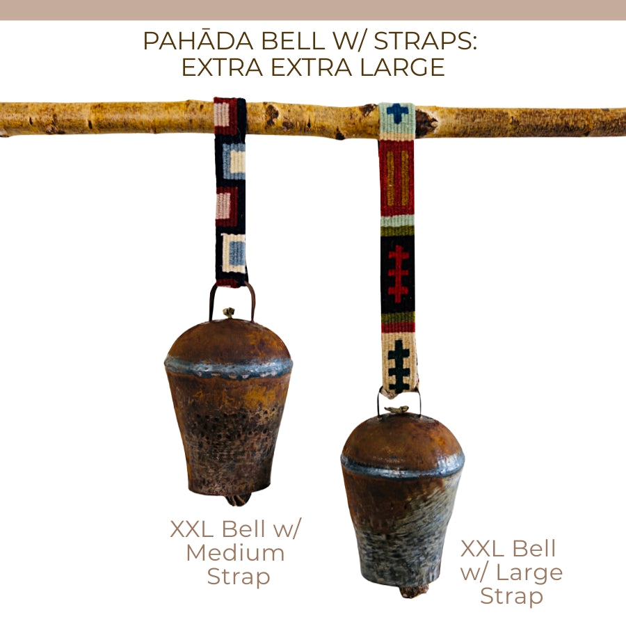 Two vintage handmade Pahāḍa bells from the Himalayan mountains of Nepal and Tibet hang from a branch, each with a colorful patterned strap. Perfect as Christmas ornaments, wreath decor, or for sound baths; each bell measures 11".