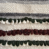 The Faino Wool Statement Bed Blanket showcases handcrafted cream, green, and brown textured patterns in horizontal stripes—an eye-catching piece for any room.