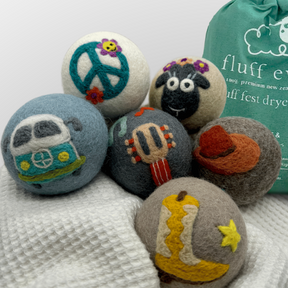 Six premium Fluff Ewes "Fluff Fest" wool dryer balls, inspired by music festivals, rest on a white towel near a green Fluff E bag—a stylish, sustainable upgrade to your laundry routine.