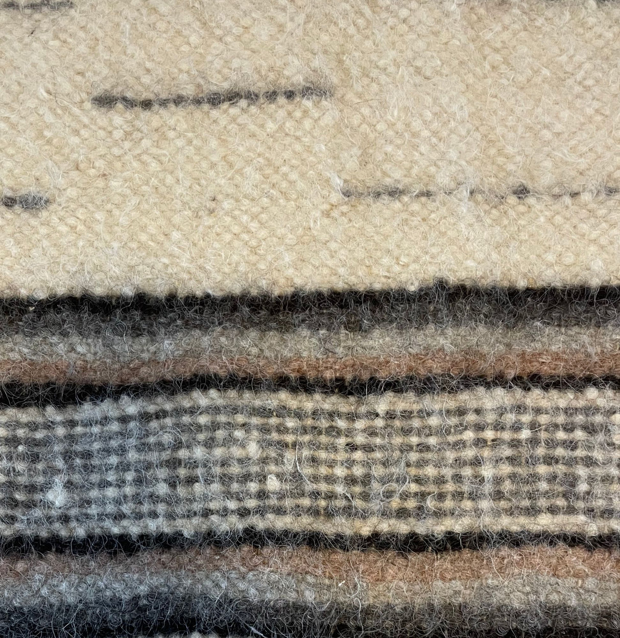 Close-up of the Gratsia (Grace) Wool Statement Bed Blanket, handwoven from organic wool with beige, brown, and gray horizontal stripes and a textured pattern.