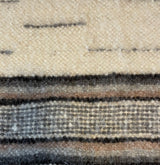 Close-up of the Gratsia (Grace) Wool Statement Bed Blanket, handwoven from organic wool with beige, brown, and gray horizontal stripes and a textured pattern.