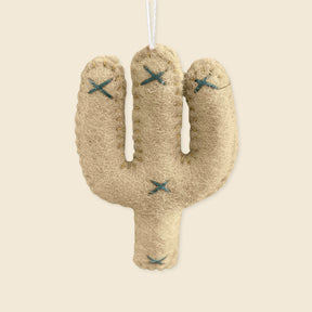 The Hand-Stitched Felted Cactus Ornament is a beige, handmade felt decoration with blue stitched details and a hanging string—expertly crafted by artisans in Nepal.
