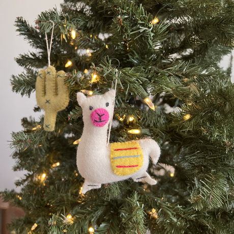 A Christmas tree shines with string lights and displays artisan decorations, including a Hand-Stitched Felted Cactus Ornament and a felt llama.