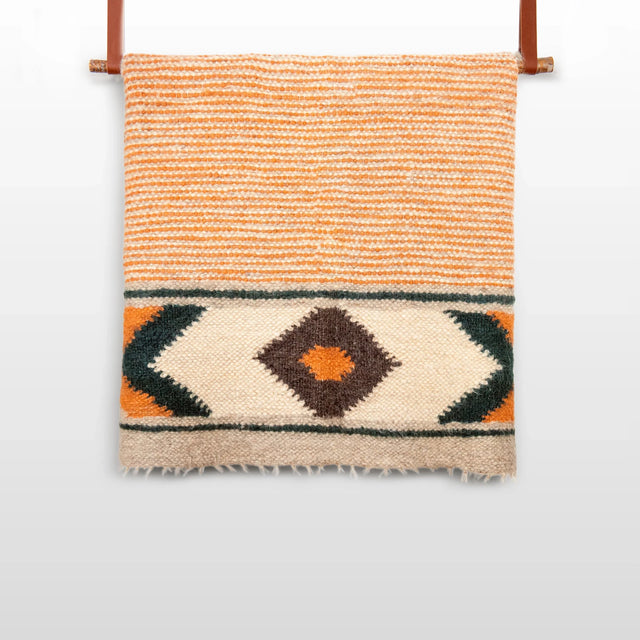 The Handmade Organic Natural 100% Sheep Wool Woven Statement Blanket features orange stripes and a geometric diamond pattern in brown, green, and orange, displayed hanging on a rod.