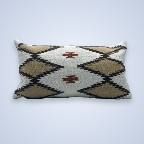 The Handwoven Blazheny (Blissful) Pillow features a rectangular shape and a geometric diamond pattern in beige, white, black, and rust on a light background.