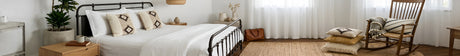 Bright, cozy bedroom with a metal bed, neutral decor, rocking chair, and natural light from sheer curtains.
