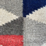 Close-up of the Harmonia B (Harmony) Wool Statement Throw / Baby Blanket, featuring red, grey, white, and blue geometric sections—a striking example of modern art blanket design.