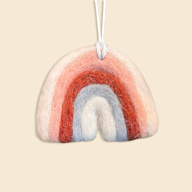 Rainbow is a hand-felted ornament with pink, red, and blue arches, crafted from New Zealand wool. Hanging by a white string against a beige background, it makes a charming addition to any artisan Christmas ornament collection.