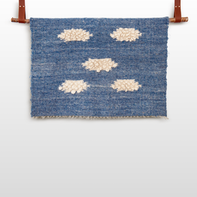 The Khmara (Cloud) Wool Statement Throw / Baby Blanket features a blue woven design with six cream-colored textured clusters, elegantly displayed from two brown leather straps.