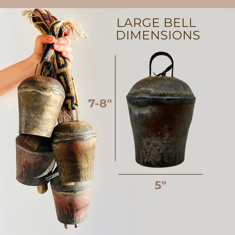 A hand holds several Vintage Handmade Pahāḍa Yak, Goat & Sheep's Bells from the Himalayas; one 7-8" tall bell is shown, ideal for Christmas ornament, wreath decor, or sound bath.