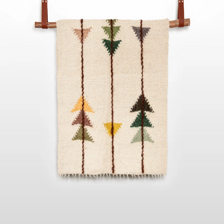 The Lis (Forest) Wool Statement Throw / Baby Blanket features a beige woven design with geometric arrow patterns in brown, green, yellow, and orange, reminiscent of handwoven art, and is displayed hanging from a rod.