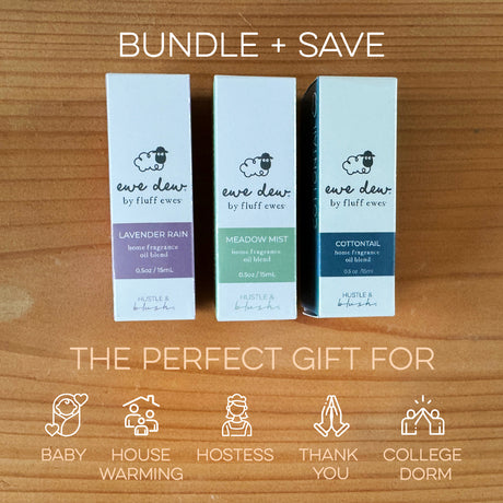 Three boxed “Ewe Dew by Fluff Ewes” Lavender Rain essential oils on a wood surface, shown as a gift bundle with ideas for use as fabric freshener, on wool dryer balls, in an oil diffuser, and more (Lavender Citrus scent).