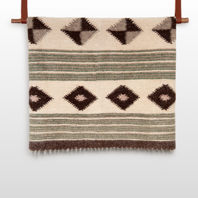 The Handmade in Ukraine Organic 100% Sheep Wool Woven Statement Blanket features geometric diamond and stripe patterns in brown, beige, and green, displayed hanging on a wooden rod.
