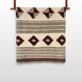 The "Handmade in Ukraine, Organic Natural 100% Sheep Wool Woven Statement Blanket Bed Covering Bedspread Duvet" features brown and green stripes with diamond patterns and hangs elegantly on a wooden rod.
