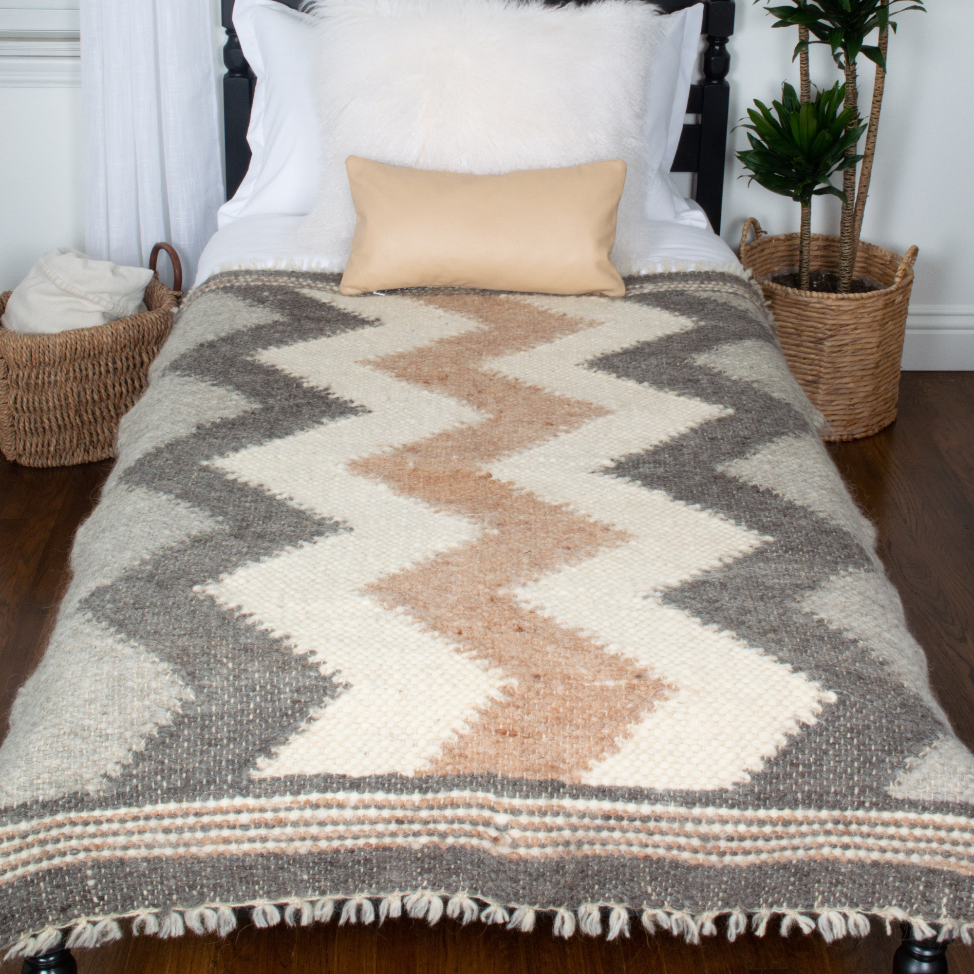 A bed with the Myr (Peace) Wool Statement Throw and a plant in a basket.