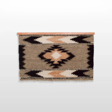 The Myr (Peace) Wool Wall Hanging is handwoven from soft Carpathian wool, featuring geometric diamond and triangle patterns in beige, black, and brown on a wooden rod.