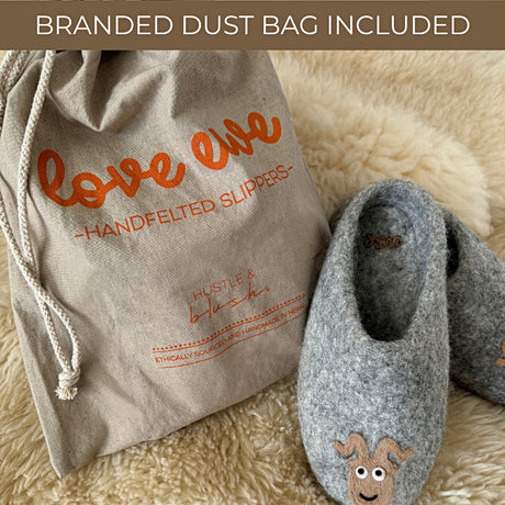 Love Ewe Hand-Felted Organic Wool Slippers for Men (Blu-G) are shown next to a branded "love ewe - Handfelted Slippers" dust bag. These handmade slippers from Nepal feature a unique design and organic wool construction.
