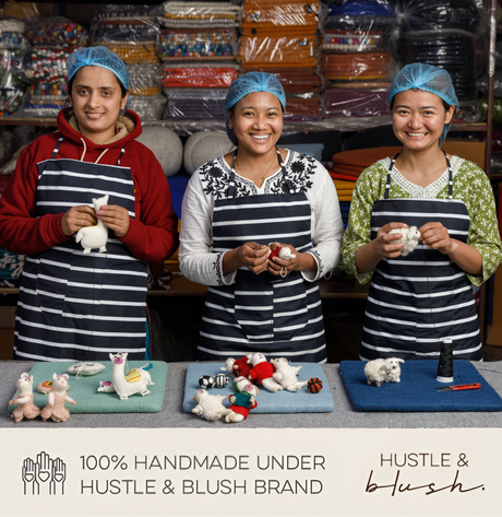 Three smiling women in striped aprons craft the handmade "Camper with Christmas Tree" felt ornament at a table, with shelves in the background.