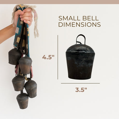 Hand holding five Vintage Handmade Pahāḍa Yak, Goat & Sheep's Bells from the Himalayan Mountains of Nepal and Tibet on a patterned strap; single 4" bell shown. Ethically sourced, handcrafted Nepal fair trade Christmas ornament or wreath decor.