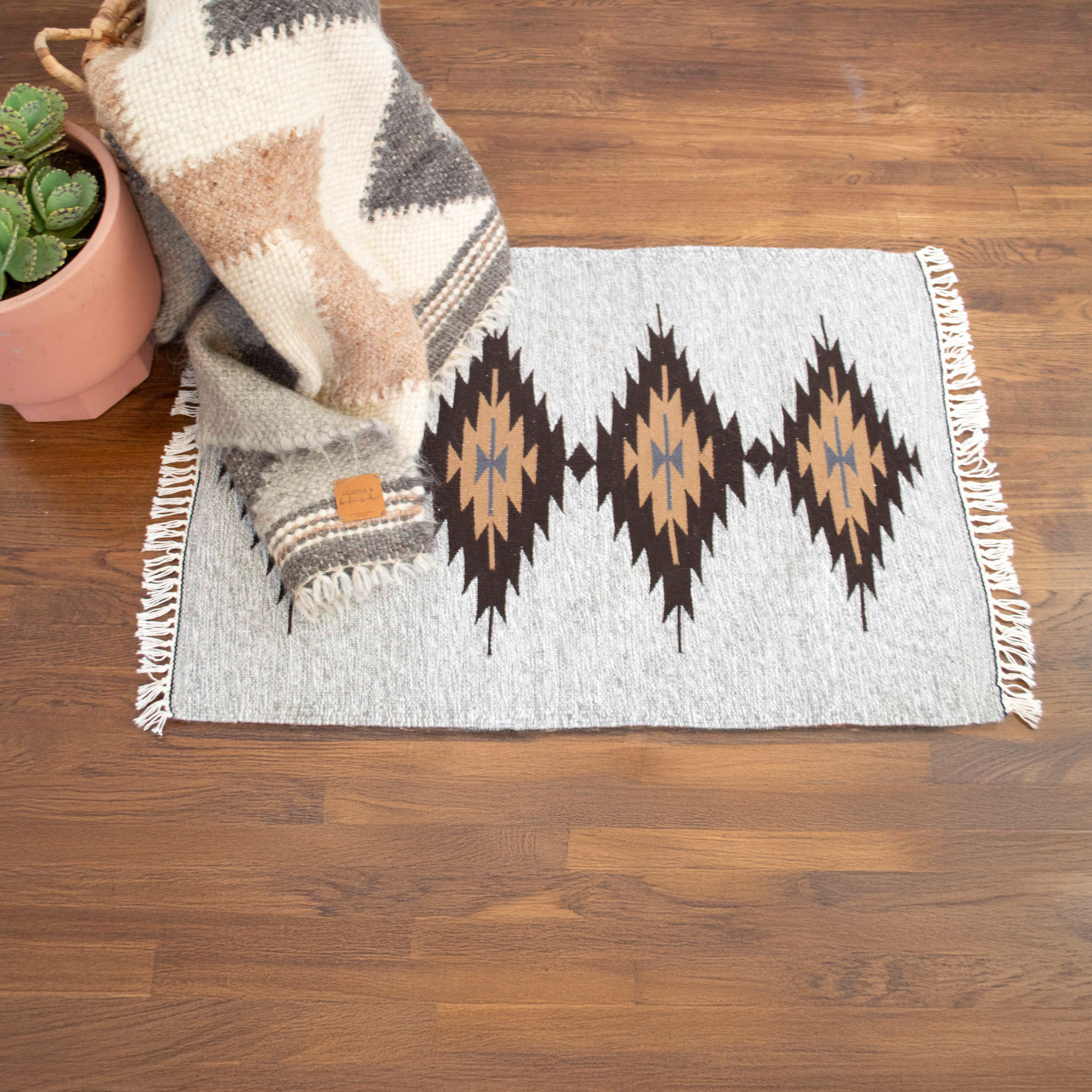 The Smilyv Wool Rug features gray neutral tones, geometric patterns, and fringed edges, bringing modern old-world style to any space as a rug or wall hanging.