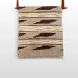 The Tak (Yes) Wool Statement Bed Blanket features beige and brown geometric patterns, handwoven from Carpathian sheep wool, and is displayed on a wooden rod with leather straps.