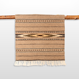 The Teplota (Warmth) Wool Small Rug / Mat - Dark features brown geometric patterns and fringe, displayed on a wooden rod—ideal as a distinctive piece of wall decor.