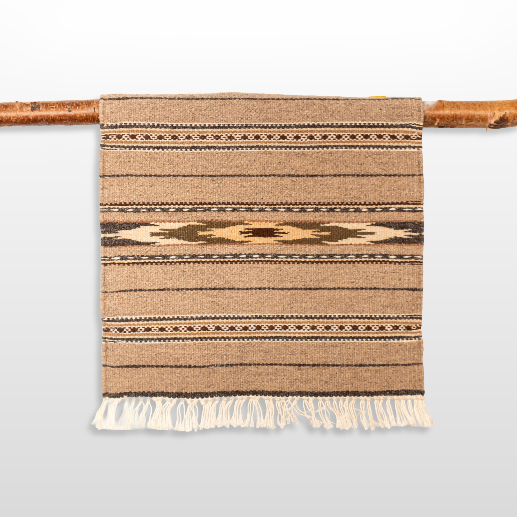 The Teplota (Warmth) Wool Small Rug / Mat - Dark features brown geometric patterns and fringe, displayed on a wooden rod—ideal as a distinctive piece of wall decor.