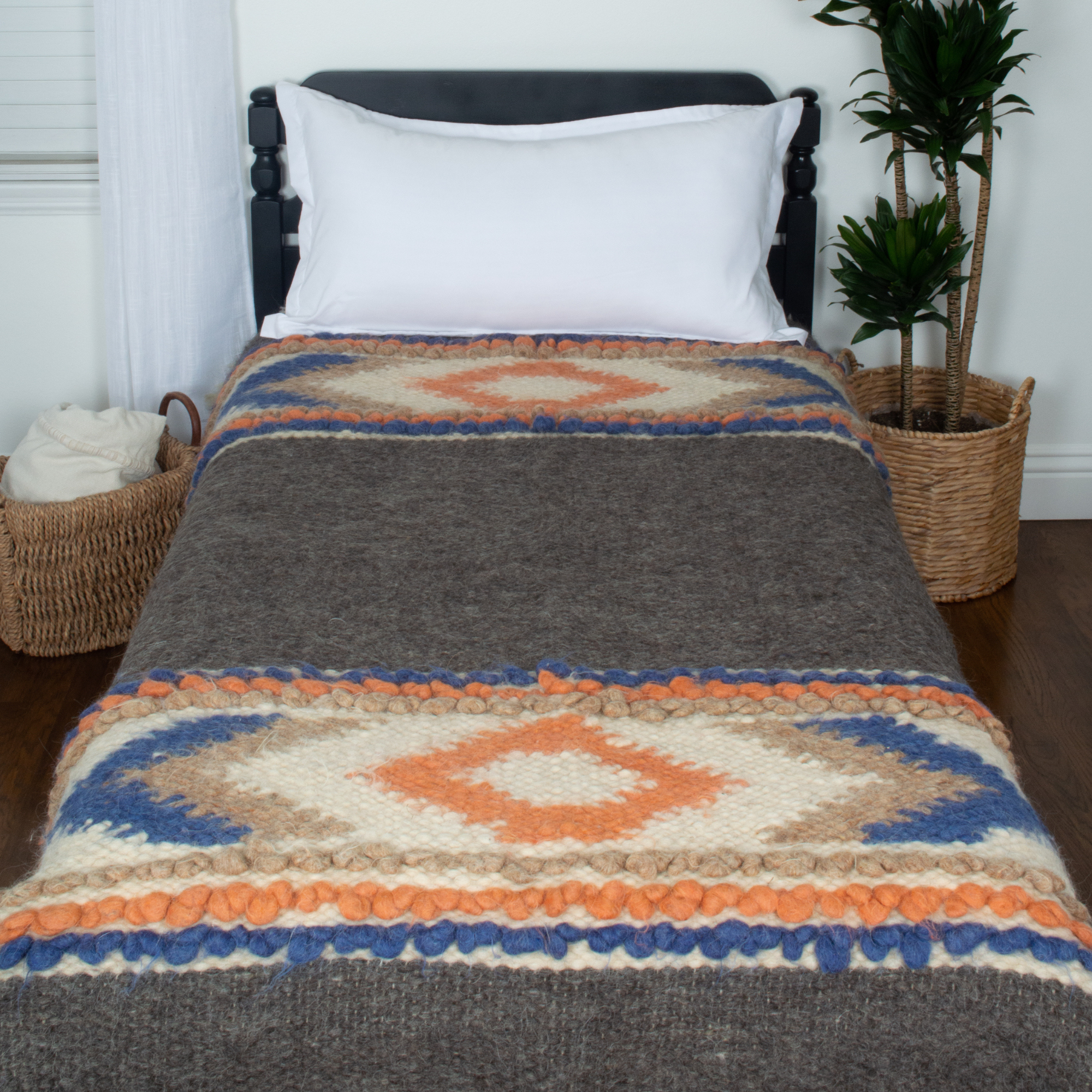 A single bed featuring the Tkach (Weaver) Wool Statement Bed Blanket in brown, orange, cream, and blue geometric patterns, next to a potted plant.