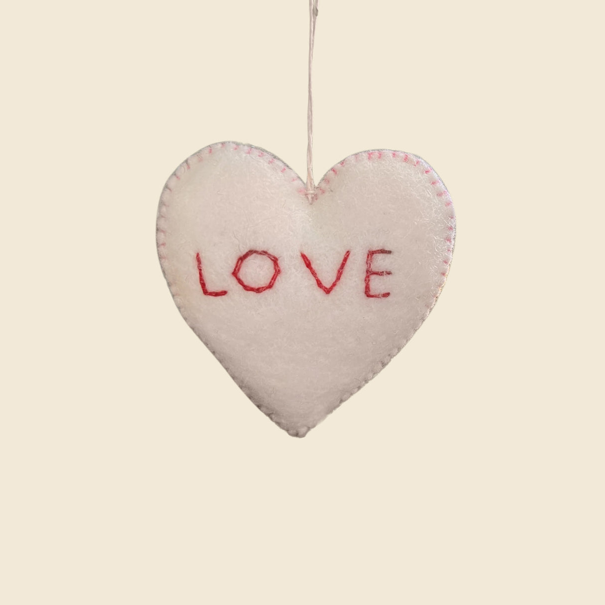 The Trio of Hand-Stitched Felt Stars and Heart Ornaments features a white wool heart with "LOVE" in red thread, hand-felted for a sustainable, artisan look. Hang these festive decorations to add charm to your holiday décor.