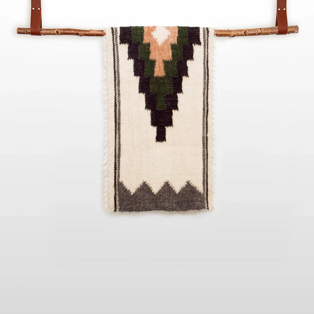 The Myr (Peace) Wool Bed / Couch Runner - Style A features handwoven geometric patterns and hangs from a wooden rod with leather straps, making it an ideal addition to sustainable home decor.