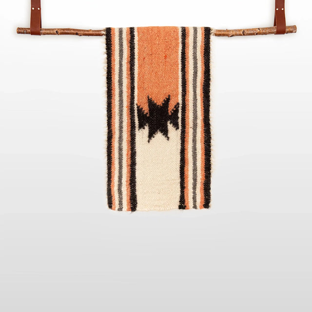 The Opora (Pillar) Wool Bed/Couch Runner, handcrafted from Carpathian sheep’s wool, features black star patterns and stripes. Hung with leather straps on a branch, it doubles as a striking bed or couch accent.
