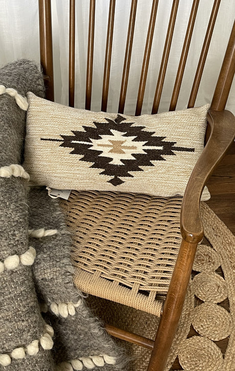 Woven chair with a geometric patterned pillow and a chunky knit blanket draped over the side.