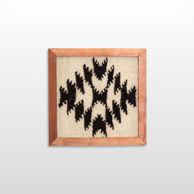 The Vira (Faith) Wool Framed Wall Art, made from undyed sheep’s wool, features a black geometric pattern on beige and is displayed against a plain white wall.
