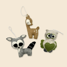 The Trio of Hand-Stitched Felted Woodland Ornaments—a raccoon, deer, and owl—each with a hanging loop, displayed on beige. Ideal artisan Christmas ornaments to add woodland charm to your holiday décor.