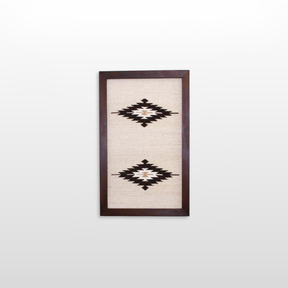 The Wool Rug Framed Wall Art showcases two black and white geometric diamond patterns on a light background, perfect for adding minimalist, eco-friendly decor to any space.