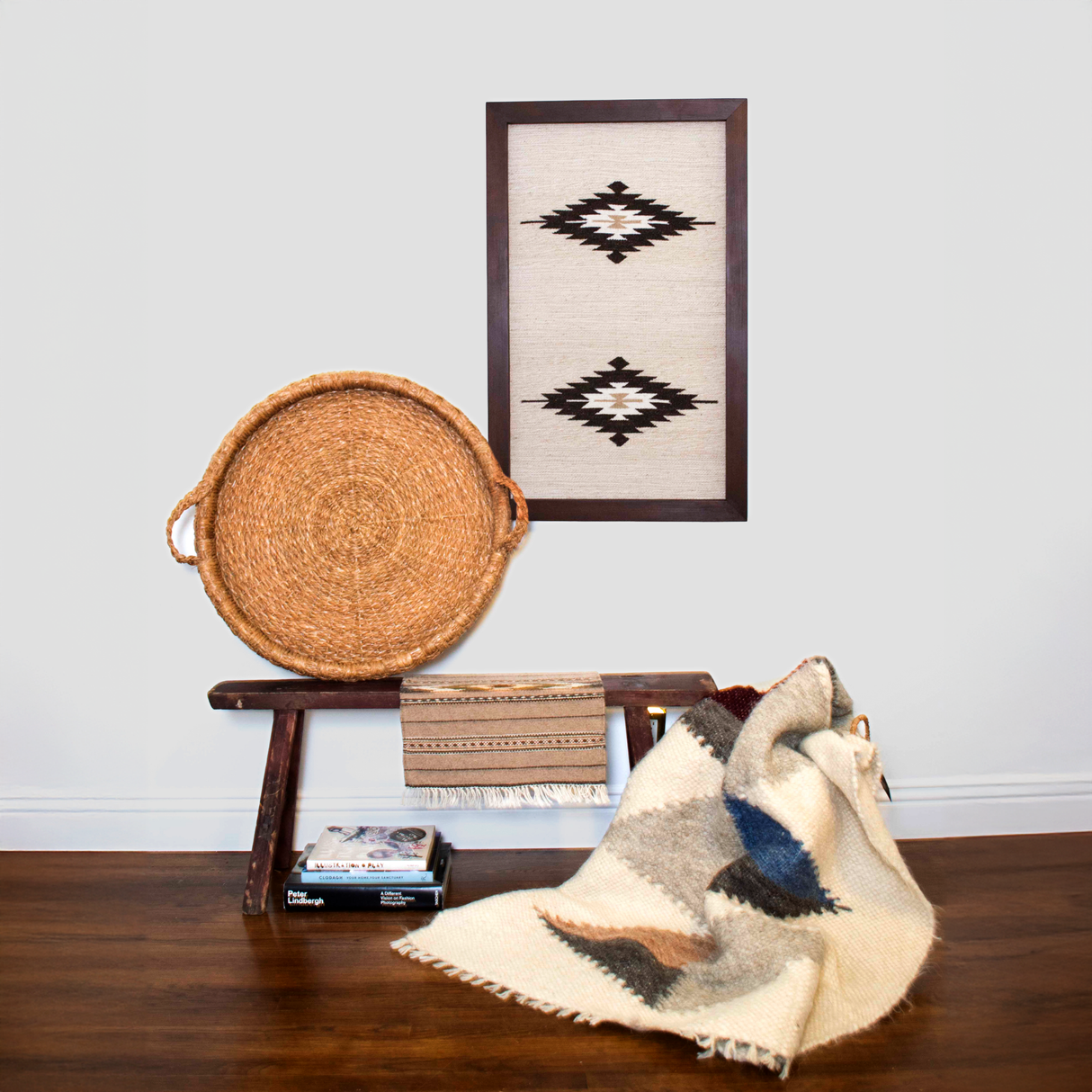 A rustic bench with a woven basket, books, textiles, and eco-friendly decor showcases Wool Rug Framed Wall Art featuring geometric patterns against a white wall.