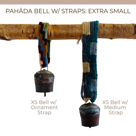 Two vintage handmade Pahāḍa yak, goat & sheep's bells from the Himalayan Mountains hang by colorful straps from a wooden branch, shown as unique Christmas ornaments or wreath decor. Each bell is 3" and perfect for sound bath use.