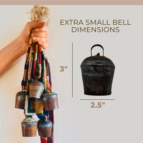 A hand holds Vintage Handmade Pahāḍa Yak, Goat & Sheep's Bells from Nepal and Tibet, featuring a 3" tall and 2.5" wide bell on colorful cords—perfect for Christmas ornaments, wreath décor, or sound baths.