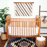 Wooden baby crib with white bedding, handwoven creation blankets, plant, woven basket, and the Promin (Beam) Wool Rug / Wall Hanging add warmth to this cozy nursery.